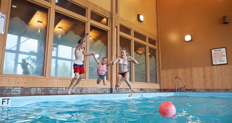 Two young children and adult jump into the indoor swimming pool.