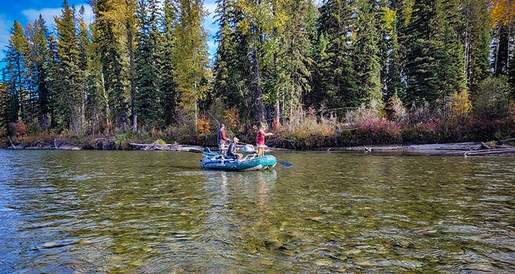 A fishing boat floats down a wide shallow river.