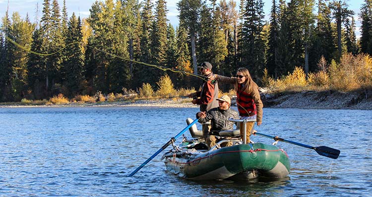 Thee people are on a boat in the water, two of them are standing and casting fishing lines.