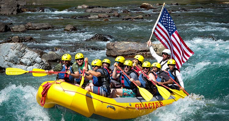 A group of rafters on the water, one is holding a large American flag.