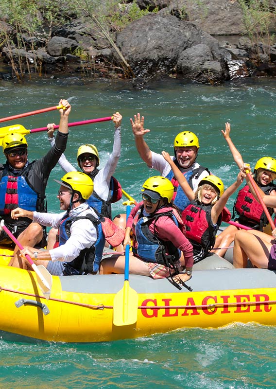 A group of rafters wave and cheer at the camera while on the water.