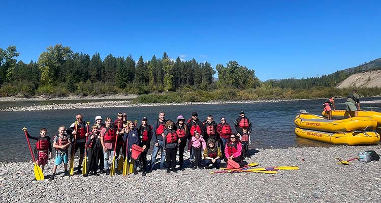 A group of people from Week of Hope posing at the riverbed with rafts to the side.