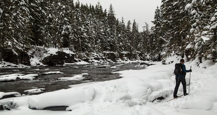 Person cross country skiing along trail beside a river