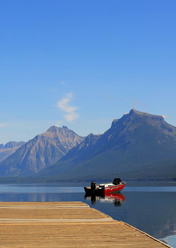 A red boat floats next to a dock at a Glacier National Park lake.