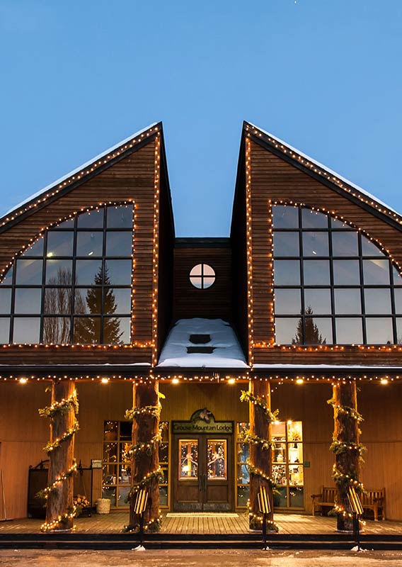 Grouse Mountain Lodge in the winter with Christmas lights adorning large windows and wooden columns