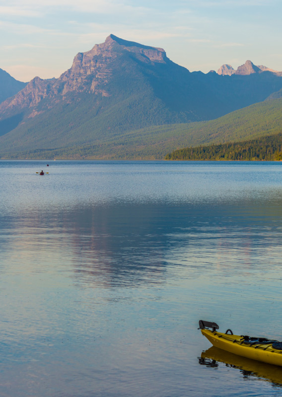 A kayak is resting on the shoreline by a lake with a mountain view