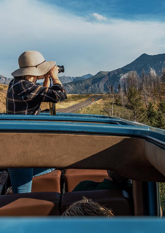 A person looks out from the open roof of an historic-style touring car.