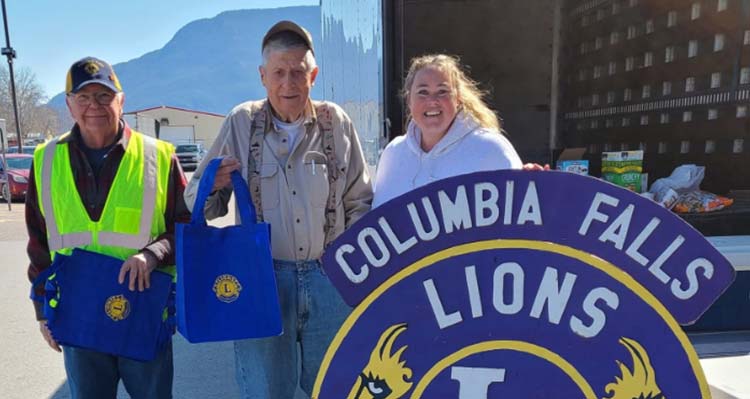 Volunteers with the Columbia Falls Lions Club pose outdoors with their sign.