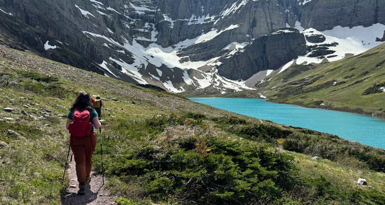 People hiking beside a river towards the mountains in Glacier National Park.