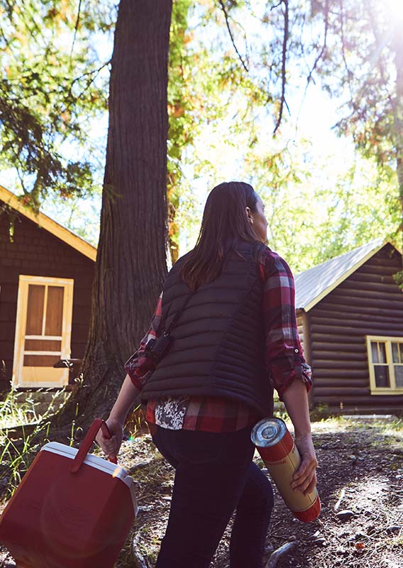 A person carrying a cooler to a group of cabins in the forest.