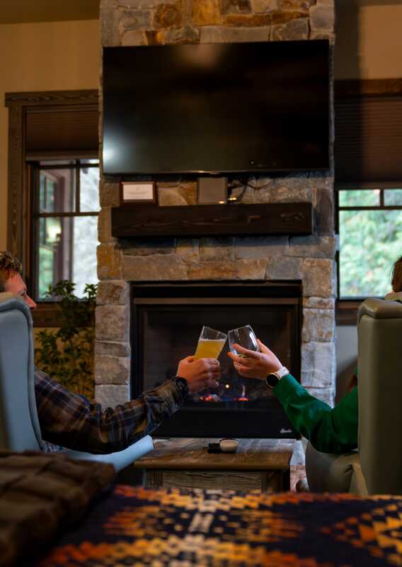 Two people make a cheers sitting by a fireplace