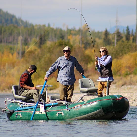 A group of anglers on a river raft, reeling in a fish.