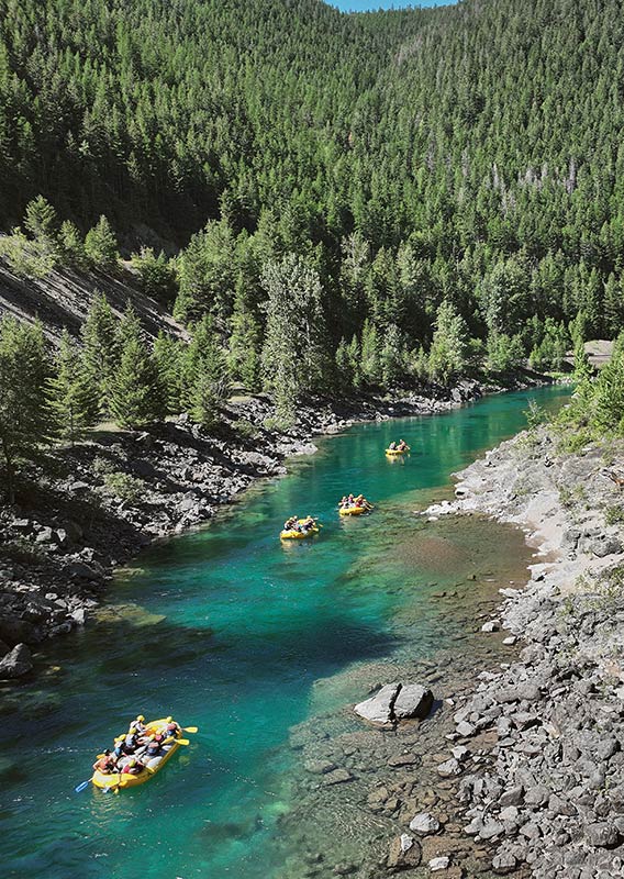 Several rafts float down a calm river with trees on either side.