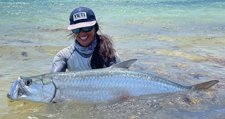 A woman holds a big fish in the water.