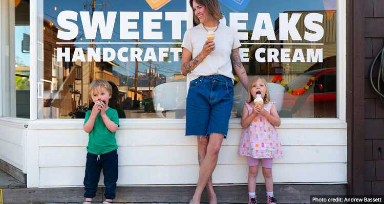 A parent and two children eating ice cream outside of Sweet Peaks Handcrafted Ice Cream shop.