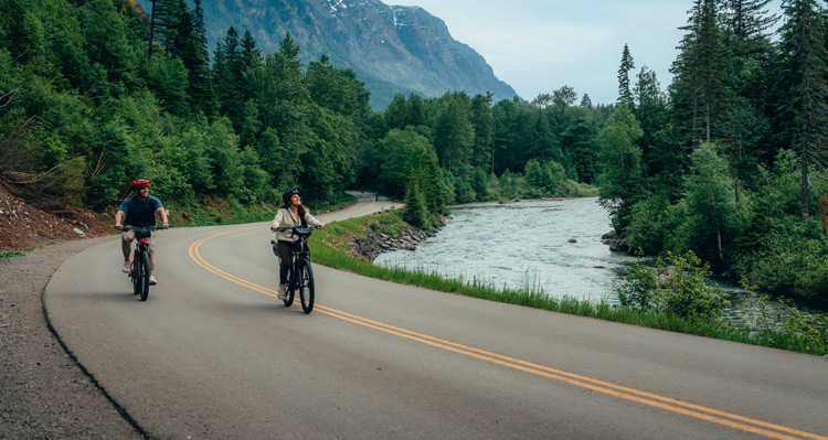Two people riding bikes beside the river in Glacier National Park.