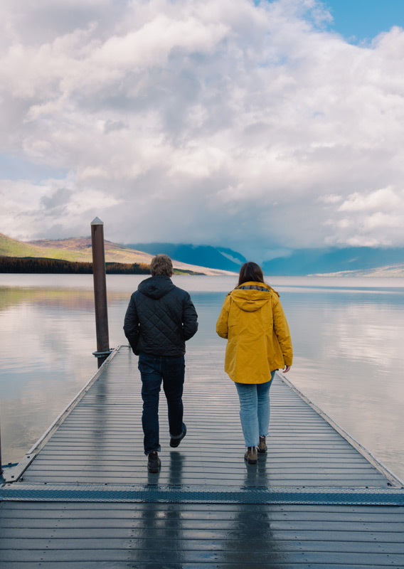 Two people walking along a dock on a lake in the fall.