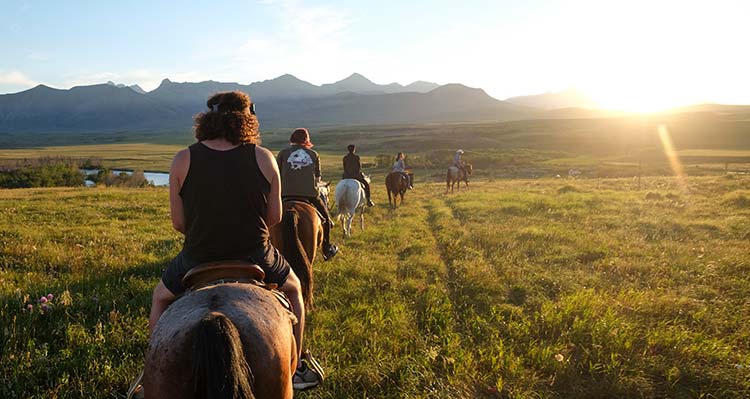 A line of people riding horses during the golden hour.
