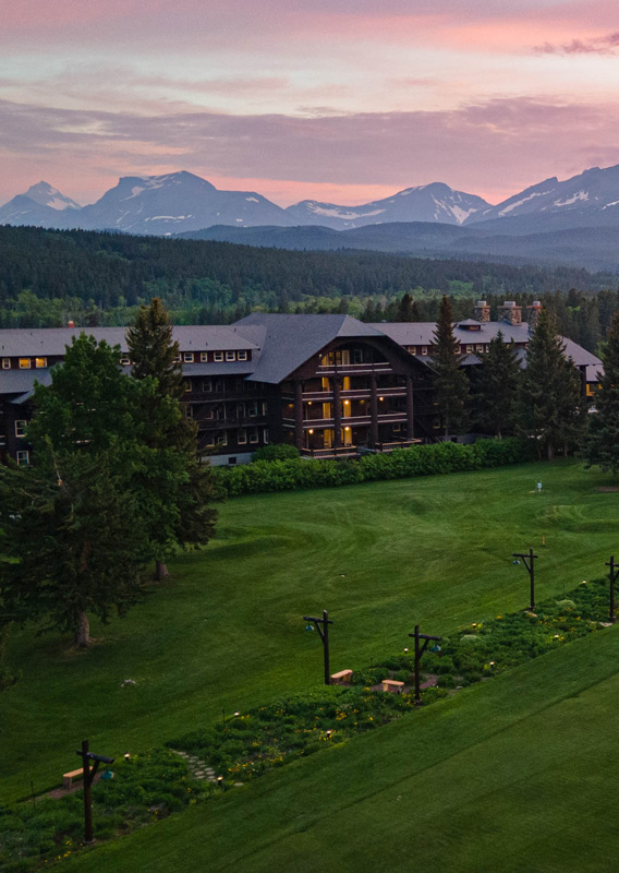 An aerial shot of the Glacier Park Lodge exterior during sunset with mountains in the background.
