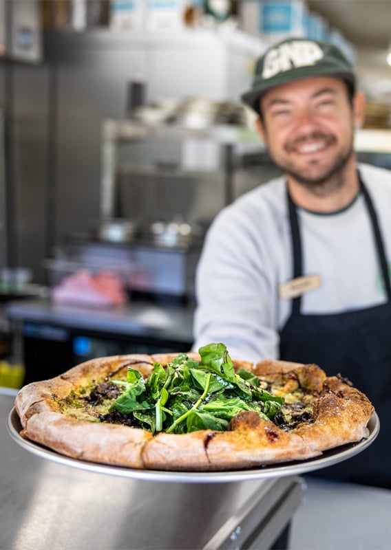 Staff member at Glacier National Pizza presenting a fresh baked pizza