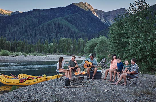A group of people sit at a riverside campfire