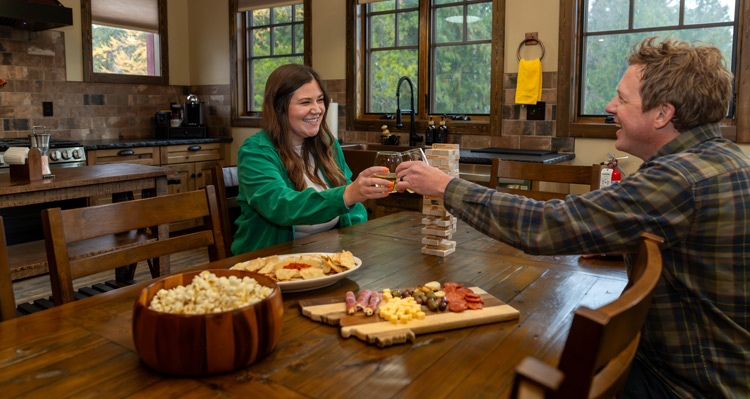 A couple toasting wine glasses with a charcuterie board on the dining table.