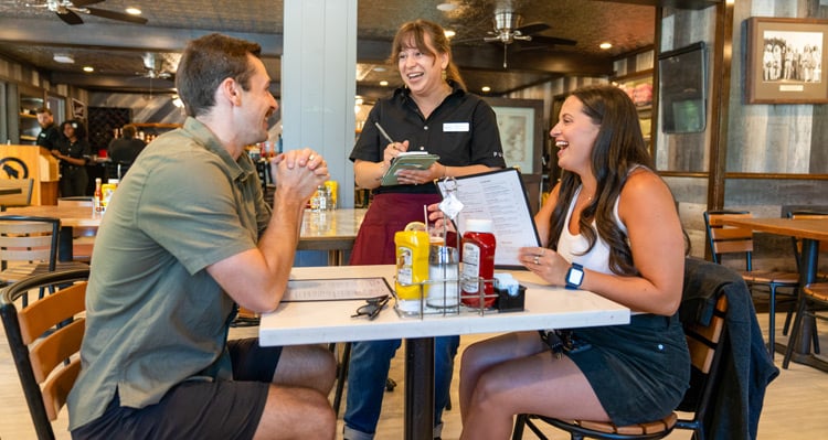 A couple seated at a table, talking with the server