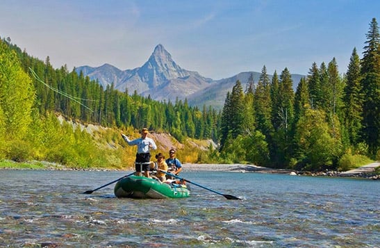 A group fly fishing on the Flathead River with a mountain view in the background