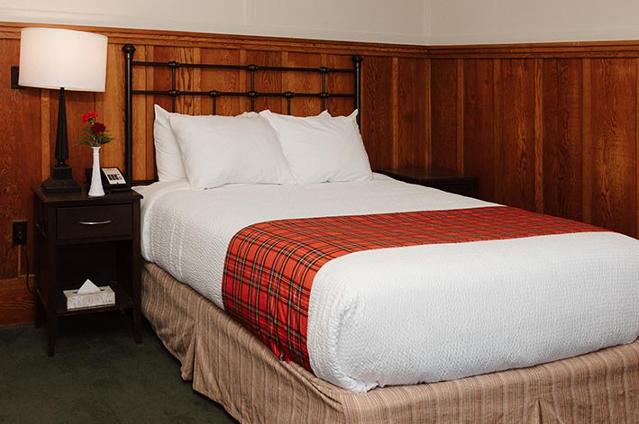 A hotel bed in a room with wooden paneling.