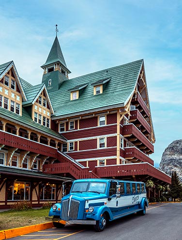 A historic touring car parked next to a large wooden hotel.