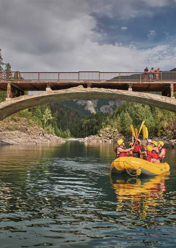 A group of rafters paddle down a river through a bridge.