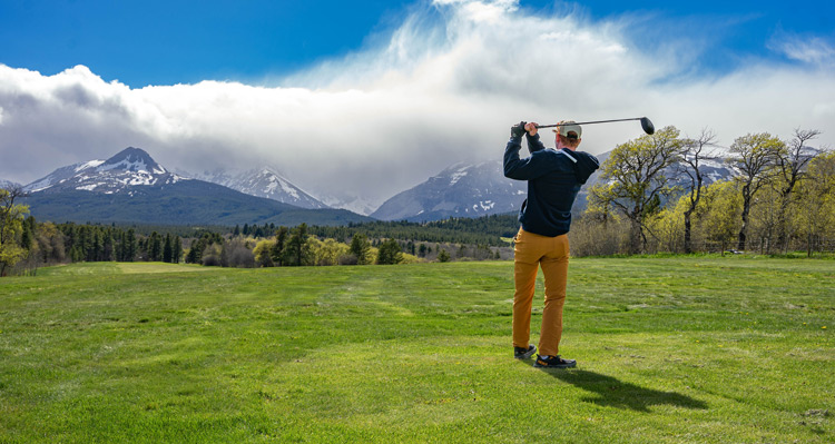 A person swinging a golf club on a course with a mountain view.