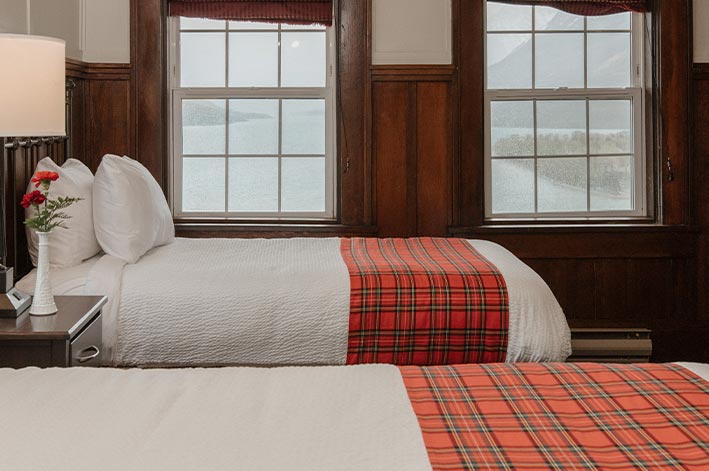 Two hotel beds next to two windows.