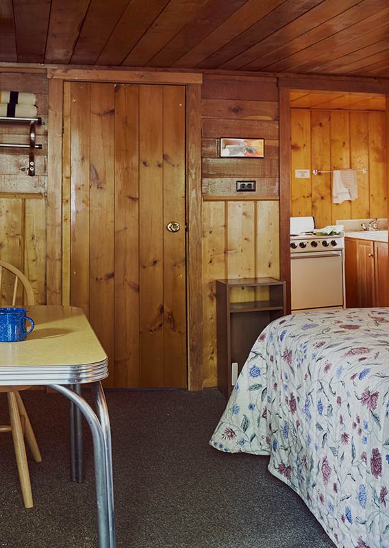 The interior of a cabin with a large bed and a kitchen in an adjacent room.