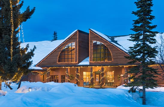 A lodge with large windows covered with snow and lights.